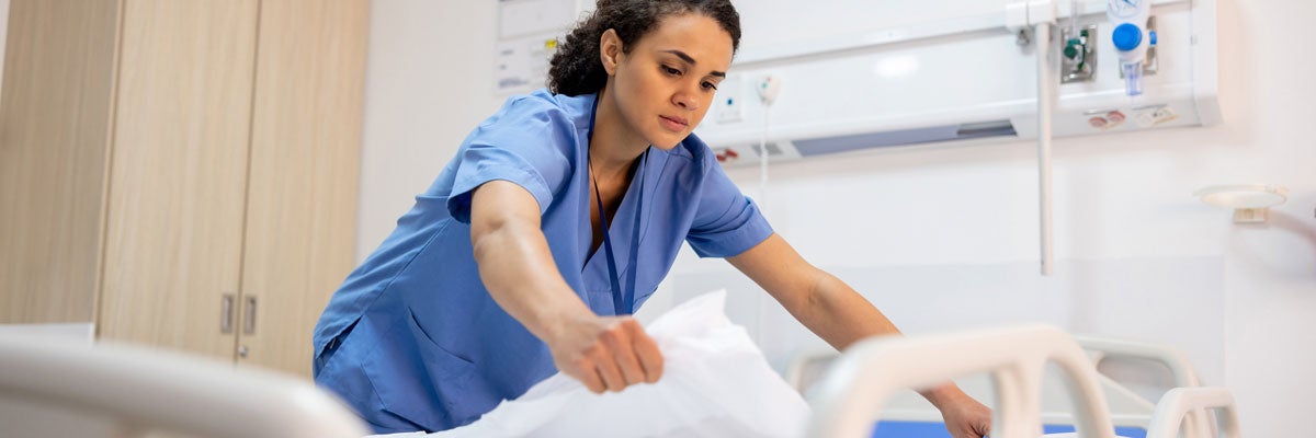 woman in scrubs making a hospital bed in a hospital room