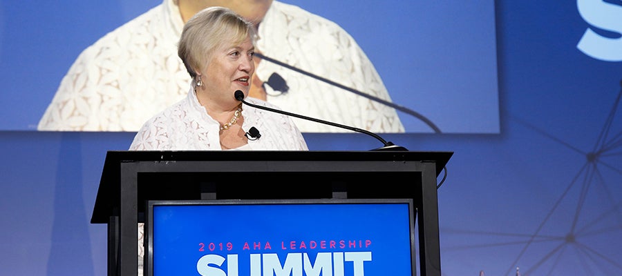 Maryjane Wurth standing at a podium speaking to 2019 AHA Leadership Summit attendees.