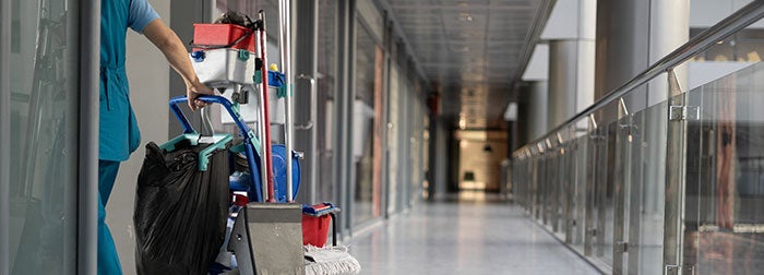 Environmental Services Technician with cleaning cart in medical hallway