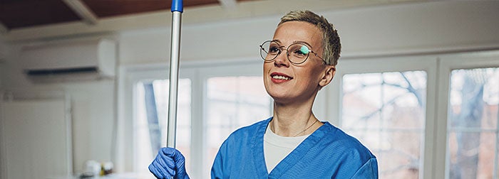 Environmental Services Technician smiling holding a mop